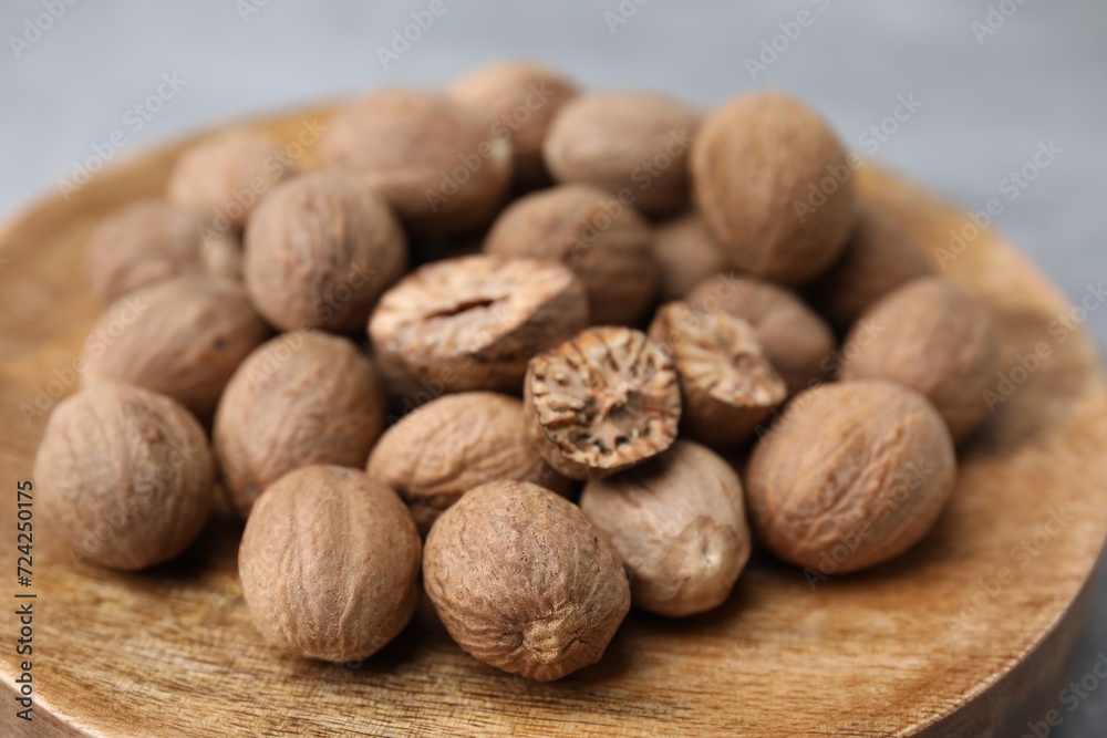 Wooden board with nutmegs on light grey background, closeup