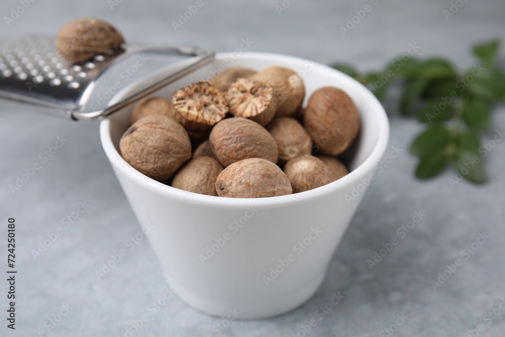 Nutmegs in bowl and grater on light grey table, closeup Nutmegs in bowl and grater on light grey table, closeup
