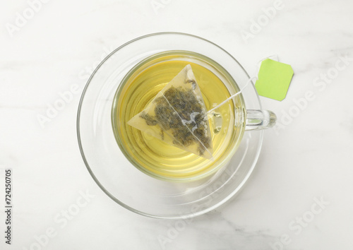 Tea bag in glass cup on white table, top view