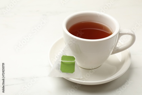 Tea bag and cup of hot beverage on white table, space for text