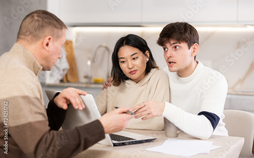 Couple young woman and young guy discussing deal with male agent in kitchen at home