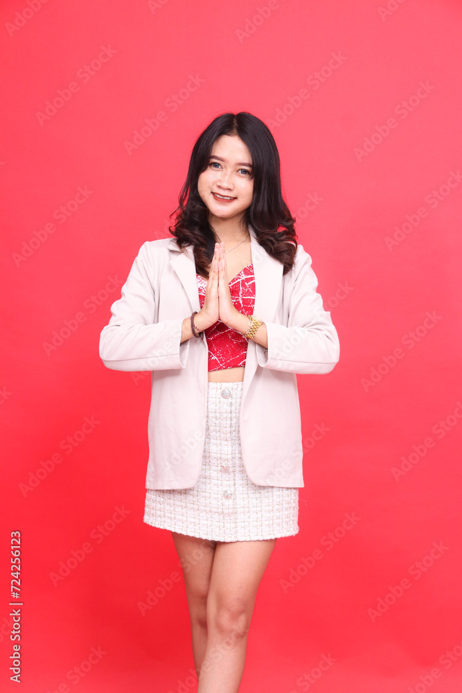 Portrait of a young Asian Indonesian woman smiling welcome wearing a cream-colored blazer. Isolated red background for content materials, banners, advertising. Portrait of a young Asian Indonesian woman smiling welcome wearing a cream-colored blazer. Isolated red background for content materials, banners, advertising.