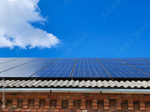 Blue solar panels on an eco-friendly house roof, harnessing the suns energy to generate clean power, creating a positive impact on the environment against a serene blue sky with scattered clouds.