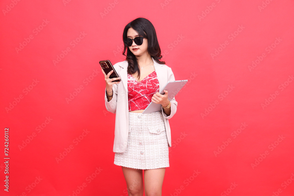 Beautiful young southeast Asian woman in sunglasses candidly looking at gadget holding tablet while wearing beige blazer Beautiful young southeast Asian woman in sunglasses candidly looking at gadget holding tablet while wearing beige blazer
