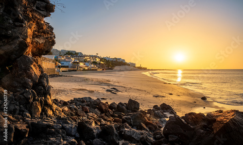 View of a beautiful sunrise light over the volcanic beach Morro Jable framed by the dark lava rocks in the summertime in Fuerteventura, Canary Islands, Spain photo