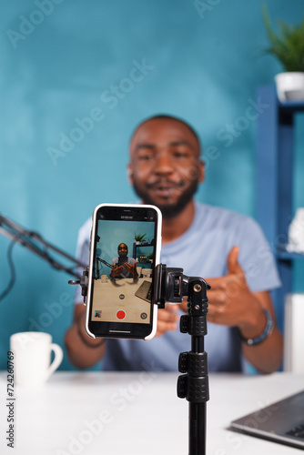 Online streamer broadcasting using smartphone on tripod close up. African american young man vlogger creating digital content and recording video for blog on mobile phone