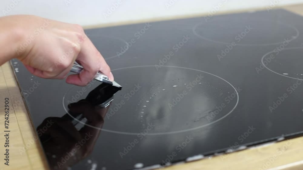 woman scraping grease from induction cooker at home woman scraping grease from induction cooker at home