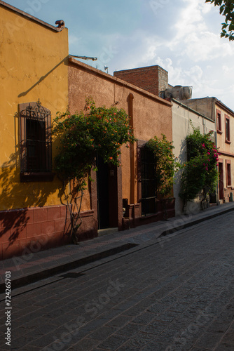 Street in the historic center of the city of Queretaro, Mexico. On this street you can see some historic or old houses while the beautiful evening sun is hitting them, outside the houses there are inc