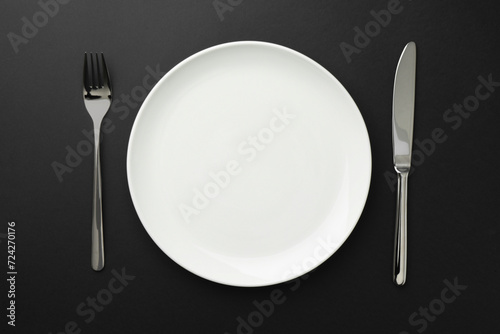 Empty plate, fork and knife on black table, top view