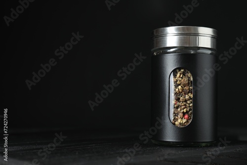 Pepper shaker on wooden board against black background. Space for text photo