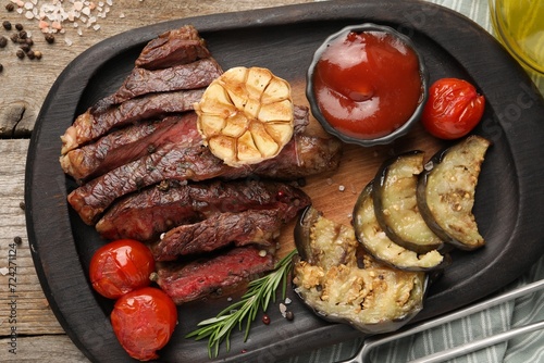 Delicious grilled beef with vegetables, tomato sauce and spices on table, top view