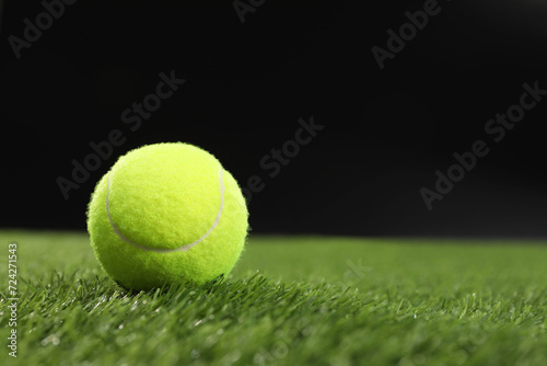 Tennis ball on green grass against black background, space for text © New Africa