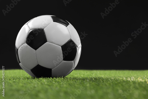 Soccer ball on green grass against black background, space for text