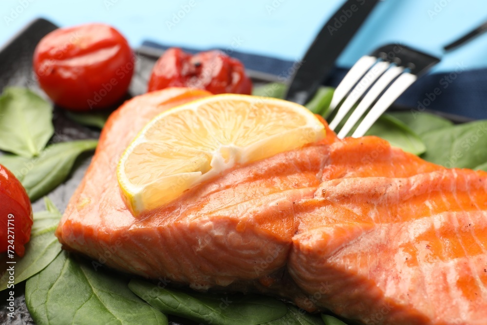 Tasty grilled salmon with tomatoes, spinach and lemon on table, closeup