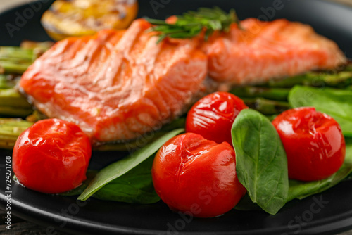 Tasty grilled salmon with tomatoes and spinach on plate, closeup