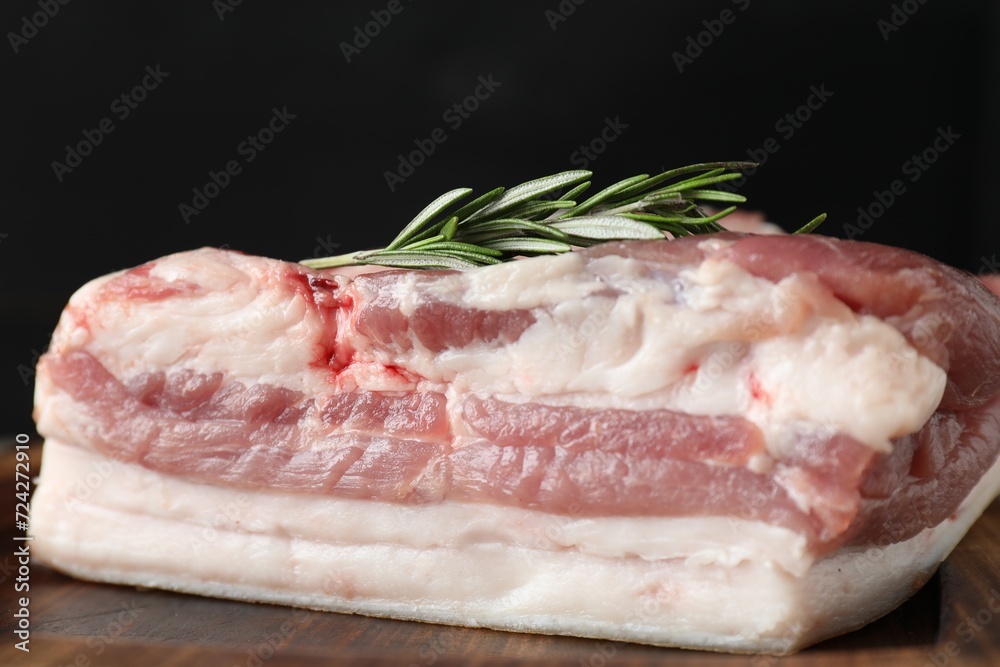 Piece of raw pork belly, salt and rosemary on wooden board, closeup