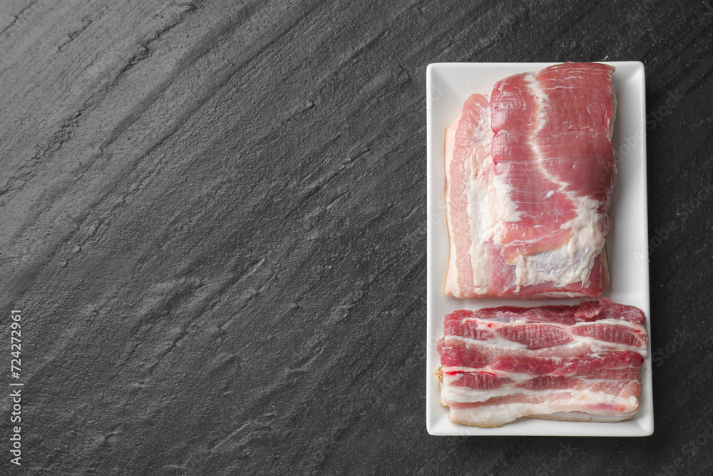 Pieces of raw pork belly on black textured table, top view. Space for text