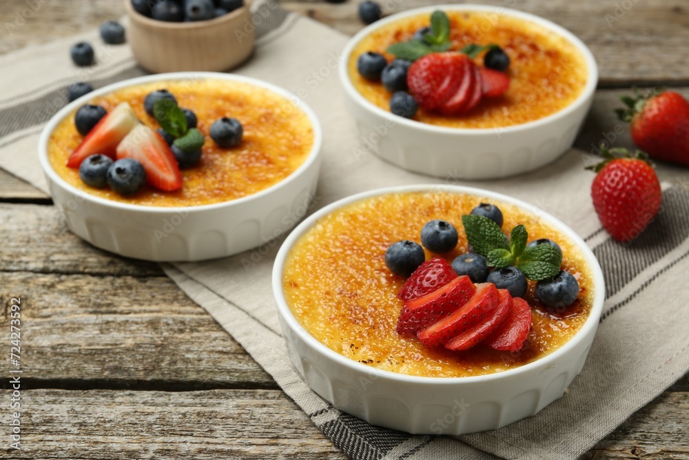 Delicious creme brulee with berries and mint in bowls on wooden table, closeup Delicious creme brulee with berries and mint in bowls on wooden table, closeup