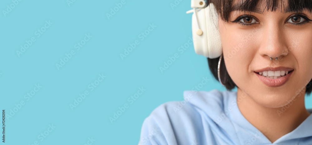 Stylish woman with nose piercing and headphones on blue background with space for text Stylish woman with nose piercing and headphones on blue background with space for text