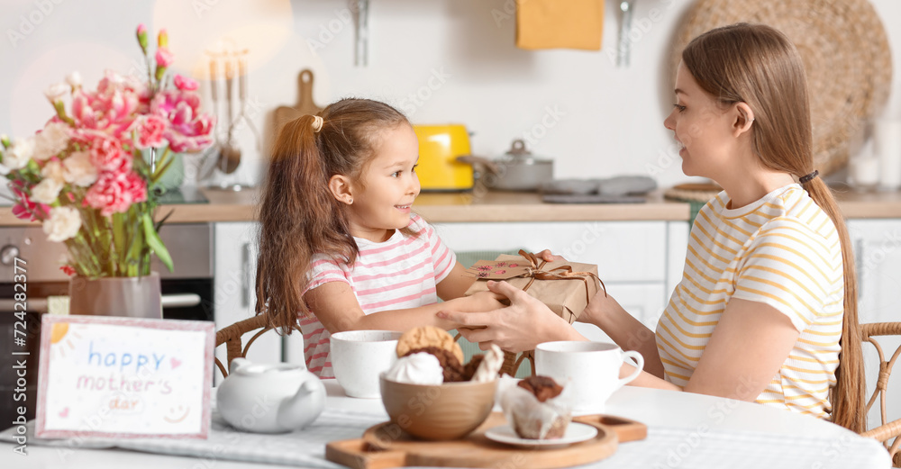 Cute little girl greeting her mother with gift in kitchen Cute little girl greeting her mother with gift in kitchen