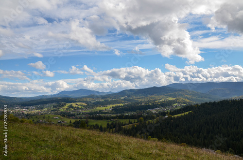 Picturesque view with high mountains covered with forests, meadows and houses scattered across the landscape, fitting well into the natural environment. Carpathians, Ukraine