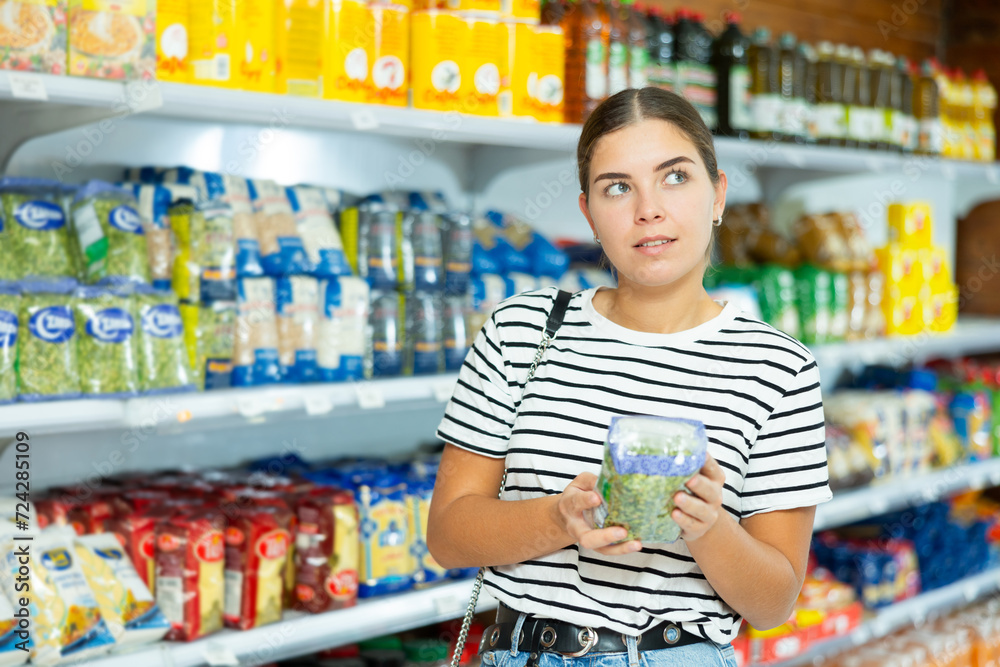 Young girl stands in cereal section of supermarket and chooses pack of peas