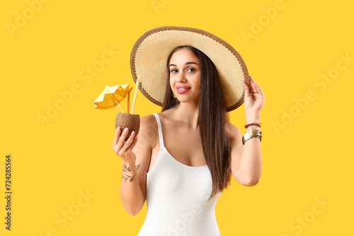 Beautiful young woman with tasty cocktail in coconut on yellow background