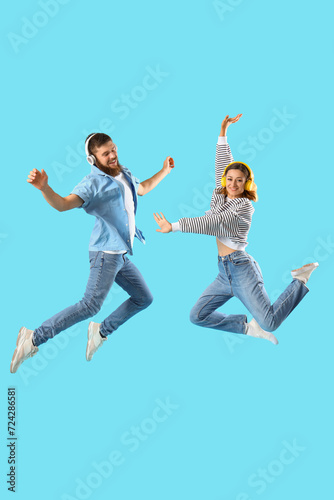 Happy couple in love with headphones jumping on blue background