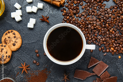 Cup of tasty coffee with cinnamon, chocolate, cookies and sugar on black background