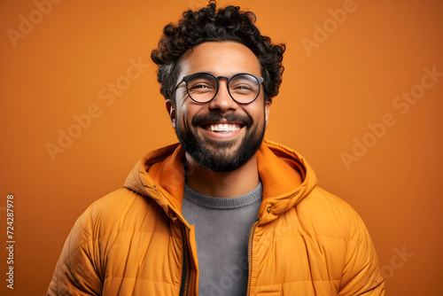 Portrait of a successful smiling bearded hispanic man in glasses on an orange background © photosaint