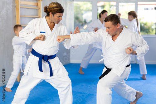 Man father is paired with male coach to learn how to strike and rehearses blocking opponent, using karate technique