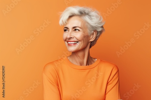 Portrait of happy senior woman in orange sweater over orange background.