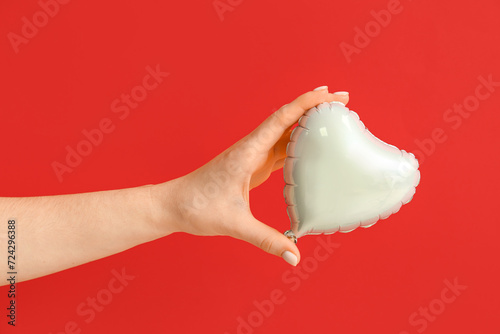 Female hand with heart shaped air balloon on red background. Valentine's day celebration