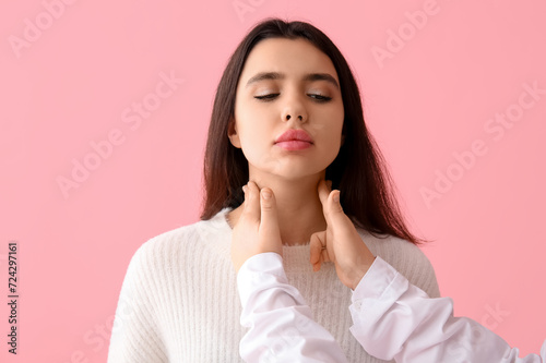 Endocrinologist examining thyroid gland of young woman on pink background