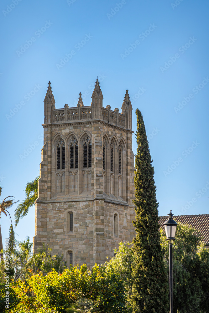 Santa Barbara, CA, USA - January 19, 2024: Trinity Episcopal Church brown stone tower above green foliage under blue sky