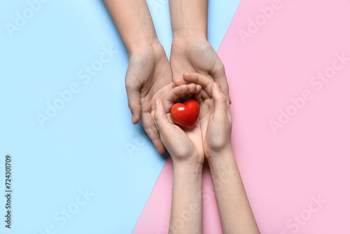 Hands of woman and child with red heart on colorful background