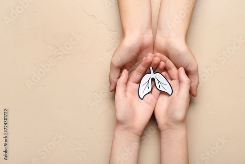 Hands of woman and child with paper lungs on beige background