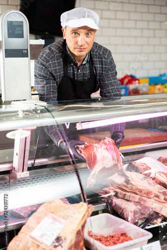 Adult male seller puts beef ribs in shop window