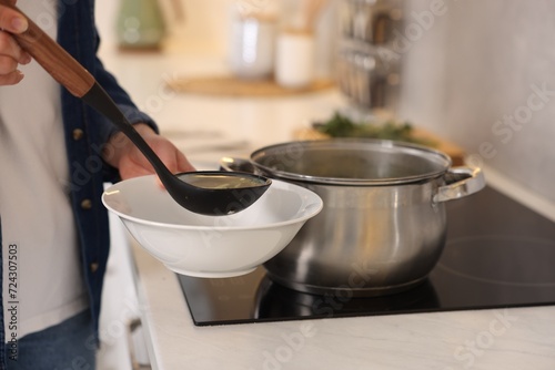Woman pouring tasty soup into bowl at countertop in kitchen, closeup