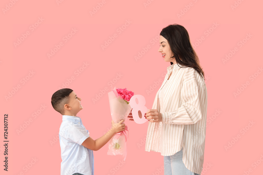 Cute little boy greeting his mother with International Women's Day on pink background Cute little boy greeting his mother with International Women's Day on pink background