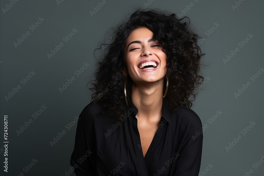 Portrait of a beautiful young woman with curly hair laughing against grey background Portrait of a beautiful young woman with curly hair laughing against grey background