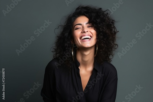 Portrait of a beautiful young woman with curly hair laughing against grey background