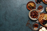 Composition with traditional Eastern sweets, tea and tasbih for Ramadan on dark color background