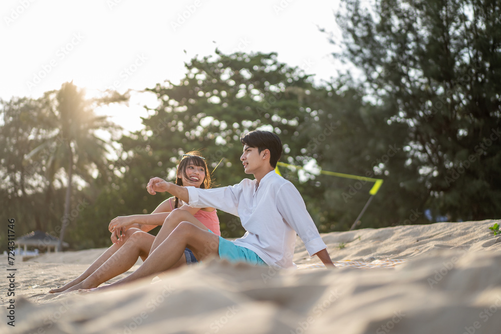 Asian young couple having picnic on the beach during summer together. 