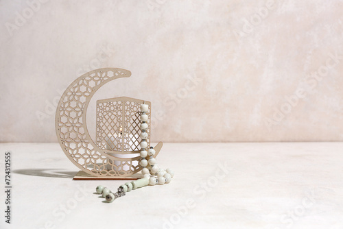 Decorative crescent with burning candle and prayer beads for Ramadan on white grunge background