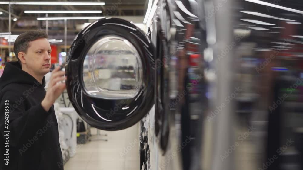 Man in the store choosing the washing machine. Open the door of the washing machine Man in the store choosing the washing machine. Open the door of the washing machine