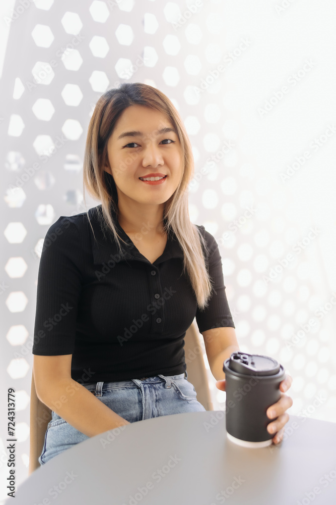 Happy Asian woman in black t-shirt sipping hot coffee in white coffee shop. Happy Asian woman in black t-shirt sipping hot coffee in white coffee shop.