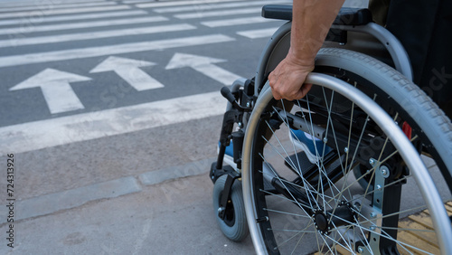 Rear view of an elderly woman in a wheelchair going to a pedestrian crossing. Close-up on wheels. 