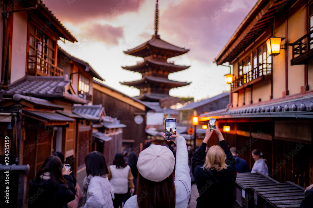Yasaka Pagoda view and Hokan-ji Temple from Yasaka Dori street in Kyoto, Japan. Popular touristic street leading to Kyomizu Dera,Young female tourist taking photo with a mobile phone during sunset. - obrazy, fototapety, plakaty 