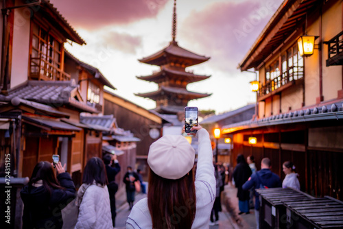 Yasaka Pagoda view and Hokan-ji Temple from Yasaka Dori street in Kyoto, Japan. Popular touristic street leading to Kyomizu Dera,Young female tourist taking photo with a mobile phone during sunset. photo